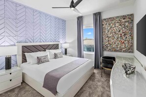Une chambre d’hôtel moderne dotée d’un grand lit, d’un bureau, d’un ventilateur de plafond, d’une fenêtre avec des rideaux et d’un grand tableau abstrait accroché au mur.