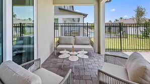 A covered patio with a sofa, two round tables, and a bottle of wine. - Rhythmic Retreat | Beach + music lover's oasis w pool, movie theater, karaoke rm (Melbourne Beach)