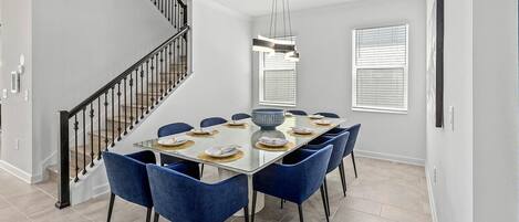 Un comedor con mesa de vidrio, sillas azules y una escalera moderna.