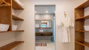 Pasillo que conduce a un baño con estantes de madera, una bata blanca colgada y un espejo sobre el lavabo.