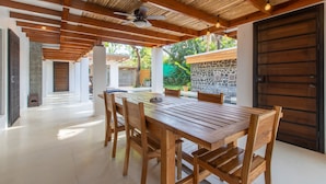 Un amplio patio con mesa y sillas de madera, un ventilador de techo y vistas al jardín.