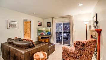 A living room with a brown leather sofa, a patterned armchair, a television, and a sliding glass door leading to an outdoor patio.