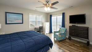 Une chambre avec un grand lit, un ventilateur de plafond, une télévision, une commode, une chaise et une fenêtre donnant sur un beau paysage.