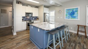 Une cuisine avec des meubles blancs, un îlot central bleu et un plancher en bois.