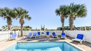 A swimming pool with blue chairs and palm trees.