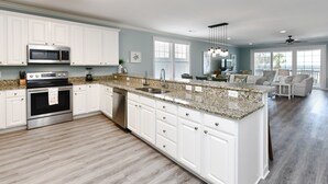 A modern kitchen with white cabinets, granite countertops, stainless steel appliances, and a large island.