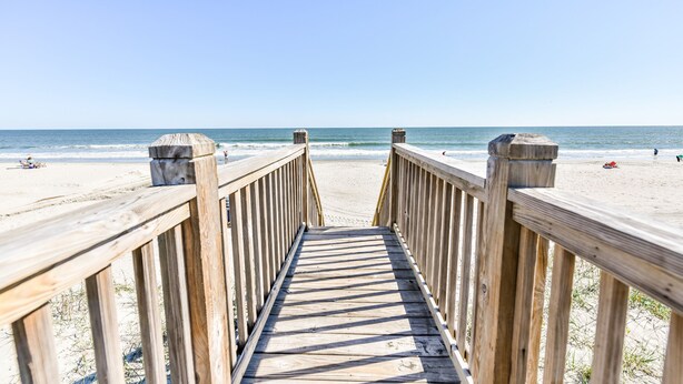 A wooden boardwalk leading to a beach with a clear sky.