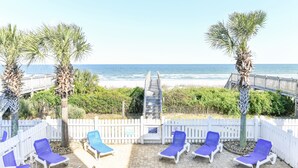 A beachside patio with lounge chairs, palm trees, and a view of the ocean.