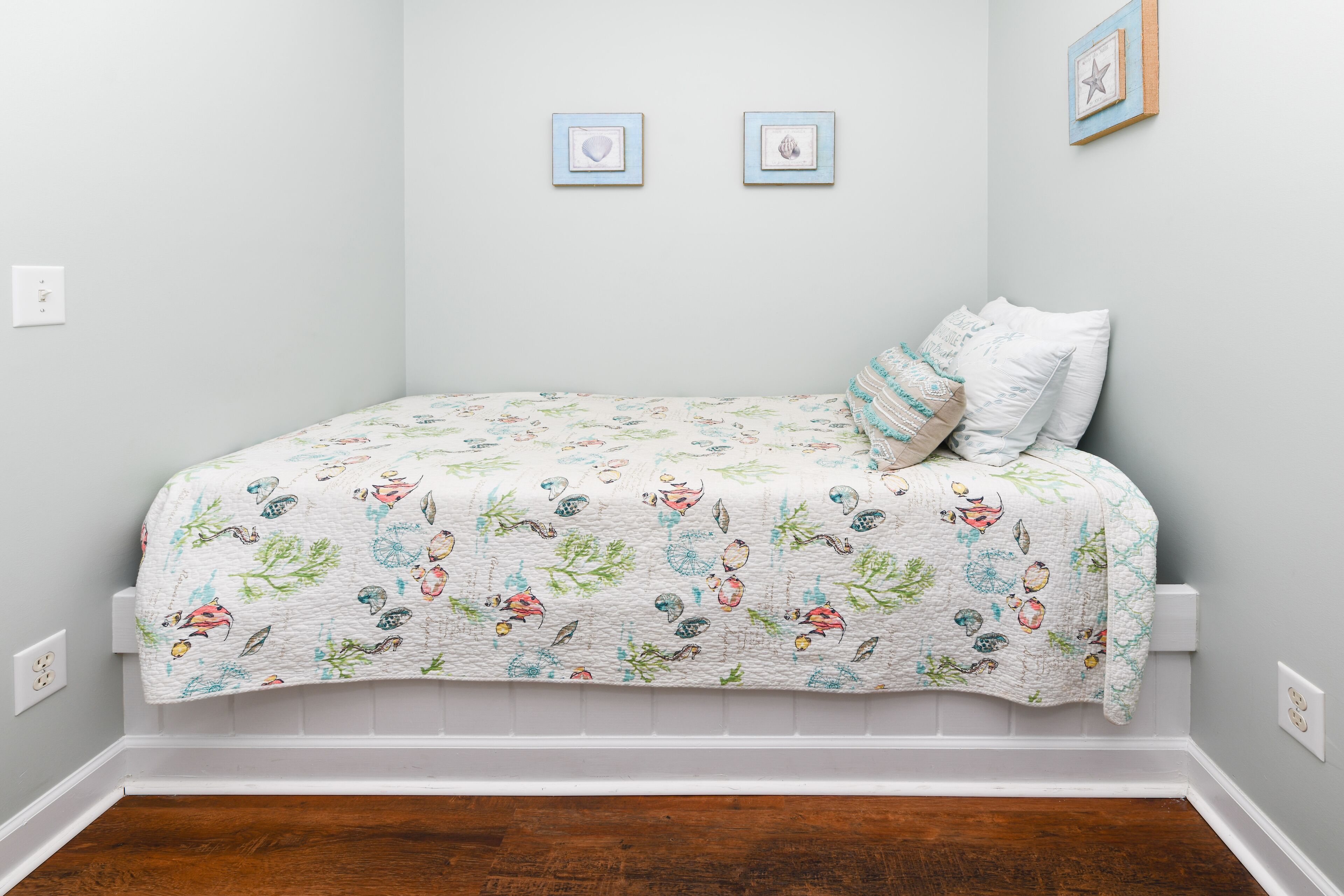 Une chambre à coucher avec un lit recouvert d’une courtepointe à motifs floraux, deux tableaux encadrés accrochés au mur et une table de chevet blanche.