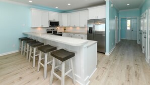 A modern kitchen with white cabinets, a stainless steel refrigerator, and a bar area with stools.