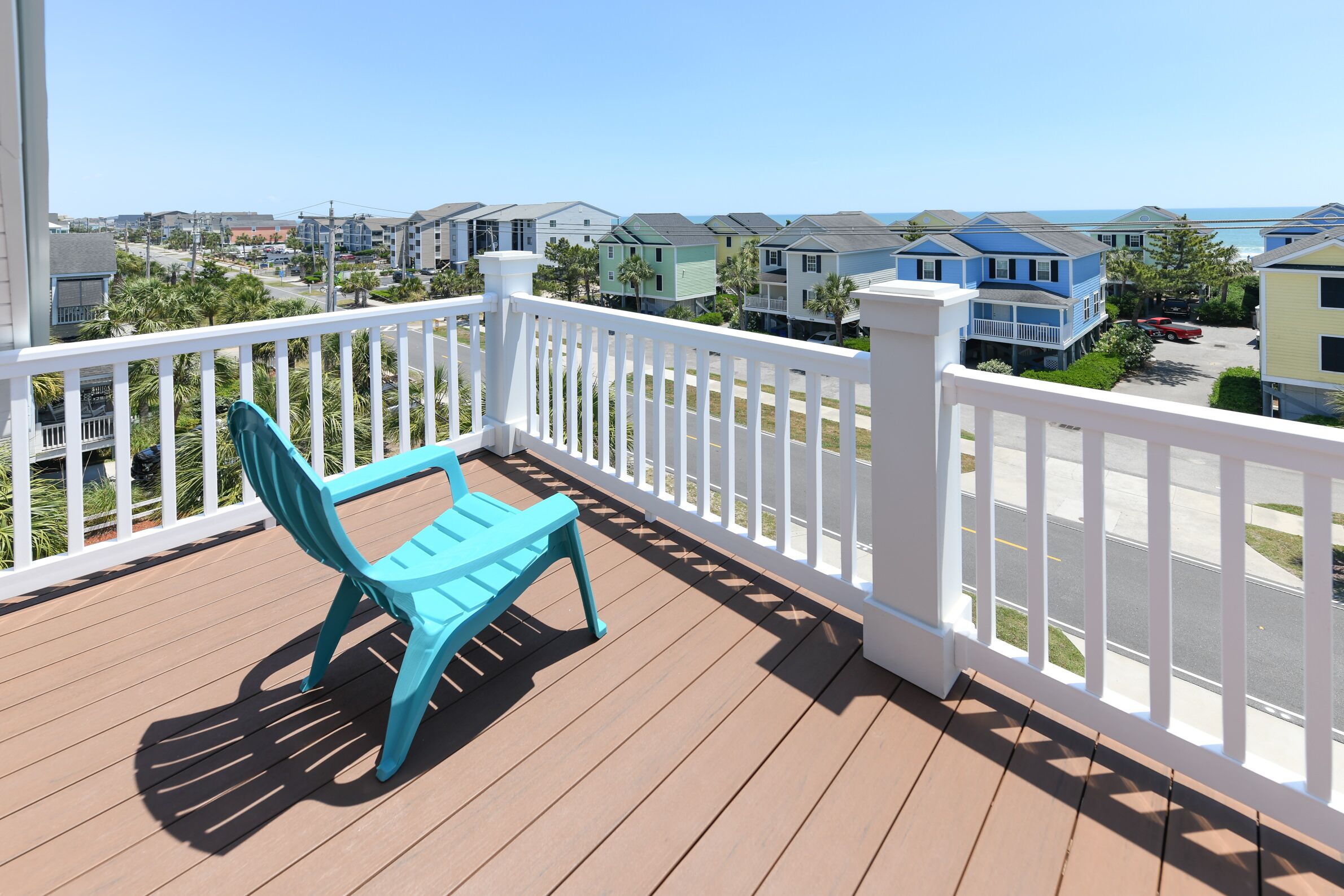 A balcony with a blue chair, white railing, and a view of colorful houses and the ocean.