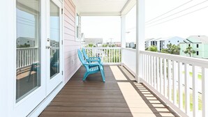 A covered porch with a wooden floor, white railings, and two blue Adirondack chairs.