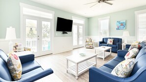A spacious living room with blue sofas, a flat-screen TV, and a ceiling fan.