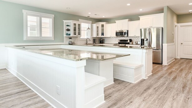 A spacious kitchen with white cabinetry, a large island, and a stainless steel refrigerator.