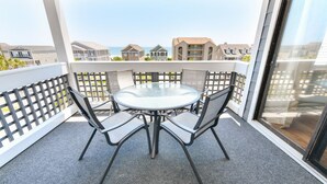 Un balcon avec une table ronde et quatre chaises, donnant sur un quartier résidentiel avec des maisons et un ciel dégagé.
