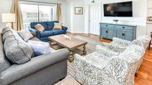 Un salon avec un canapé bleu, un divan gris et un canapé à motifs. On y trouve une table basse en bois et un téléviseur posé sur un meuble bleu.