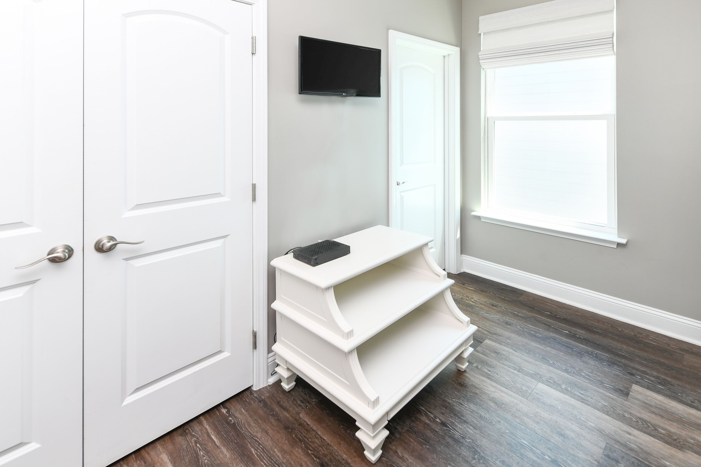 A hallway with white doors, a white console table, a mounted TV, and a window with blinds.