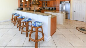 A kitchen with a central island, wooden bar stools, and a stainless steel refrigerator. - Oceanfront 7 BR Beach House with a Private Pool! Royal Palm (Garden City)