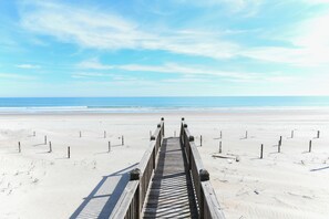 Ein Holzsteg führt zu einem Strand unter blauem Himmel.
