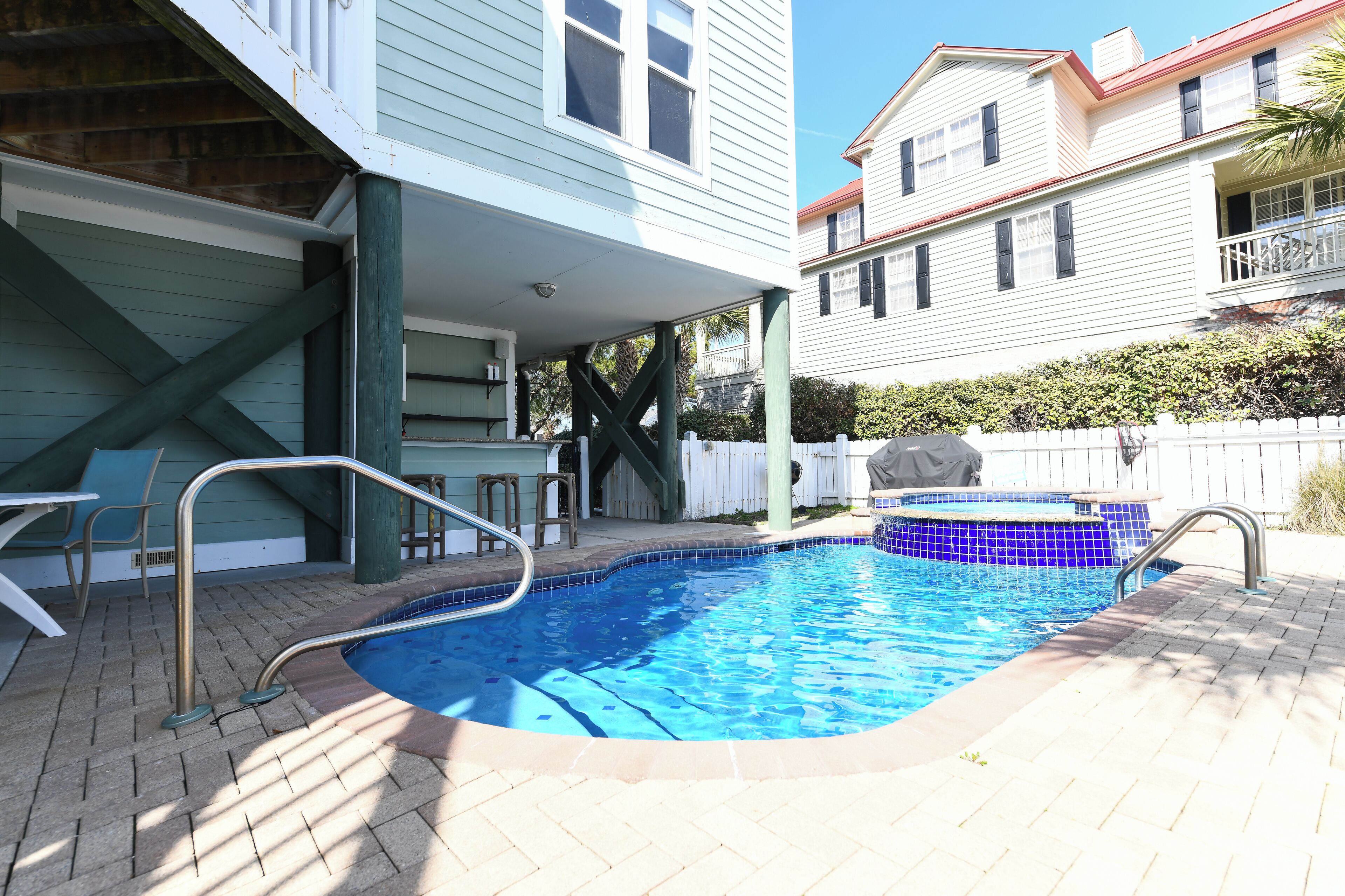 A swimming pool with a tiled edge, a covered deck area, and a white picket fence.