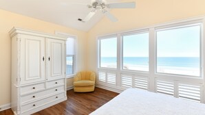 A bedroom with a large bed, a wardrobe, a chair, and a view of the beach through large windows. - Oceanfront 7 BR Beach House with a Private Pool! Royal Palm (Garden City)