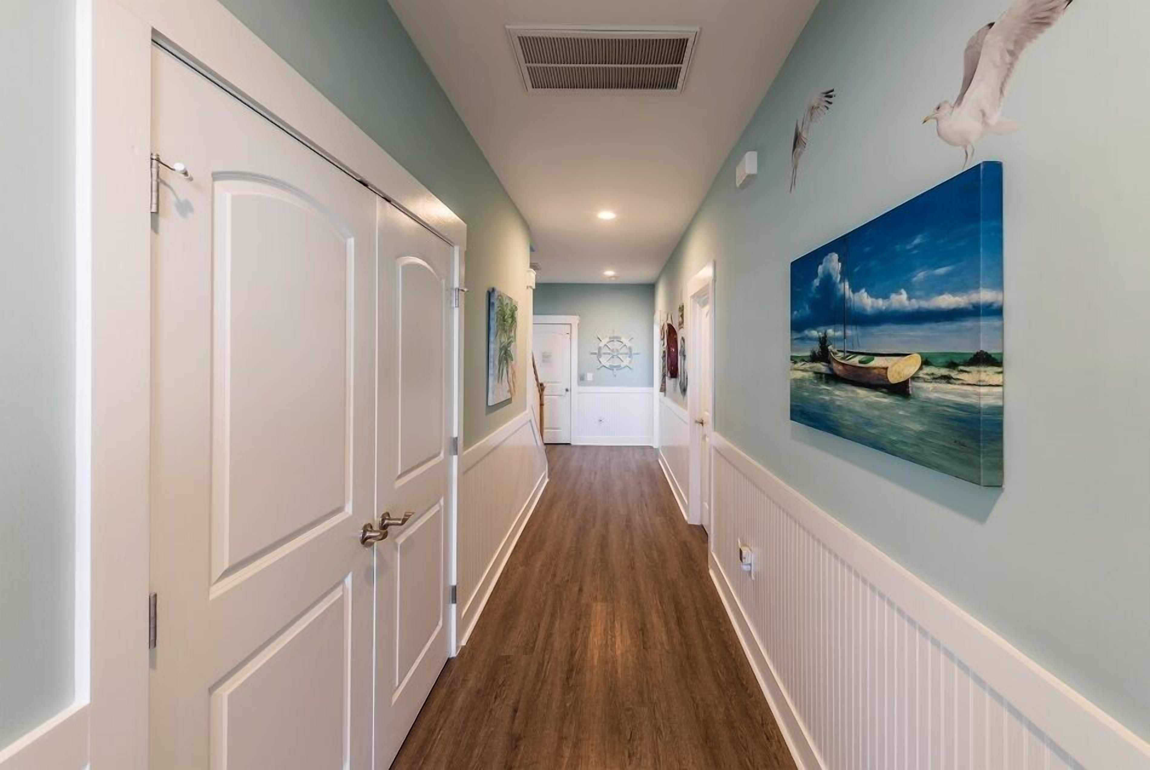 A hallway with wooden flooring, white doors, and a seascape painting on the wall.
