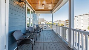 A covered porch with dark wooden flooring and white railings, featuring four wicker chairs and two wall-mounted lanterns. - Ocean View 7 BR Beach House with a Private Pool! Seaside Retreat  (Surfside Beach)