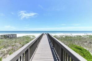 Ein hölzerner Steg führt zu einem Strand unter blauem Himmel.
