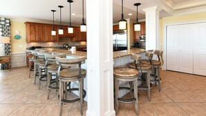 Una cocina con una isla central, taburetes de bar, armarios de madera e iluminación colgante.