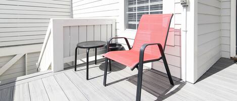 Une terrasse avec une chaise rouge et une petite table ronde, un revêtement extérieur blanc et une fenêtre avec des stores.