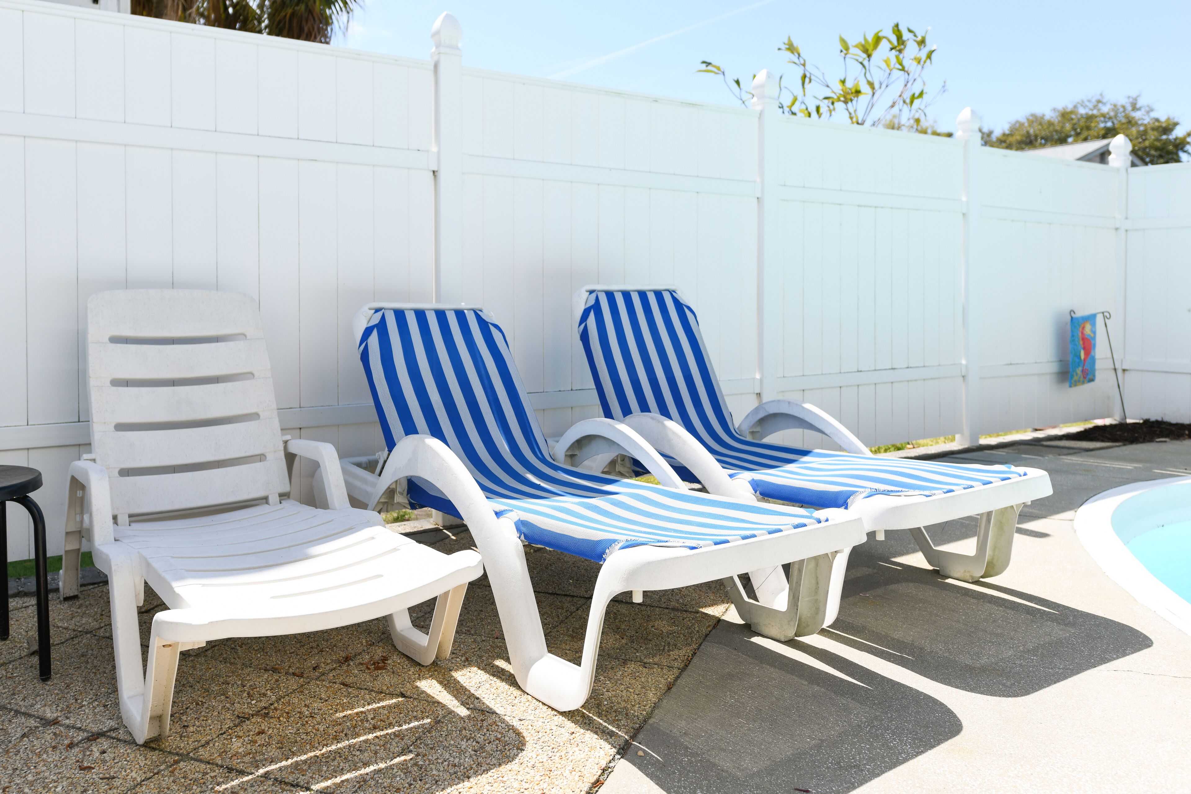 Two white lounge chairs with blue and white striped cushions, a white fence, and a pool in the background.