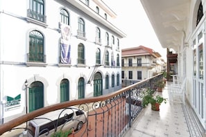 A balcony with a railing, potted plants, and a building with green shutters and a sign for 'MUSEE CANAL'.