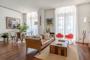 Una sala moderna con un sofá de cuero, dos sillones rojos, una mesa de centro de madera y un comedor con mesa y sillas.
