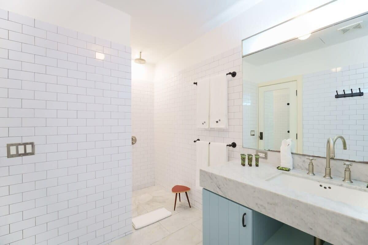 Een moderne badkamer met witte metro tegels, een grote spiegel, een marmeren aanrecht en een douchehoek.