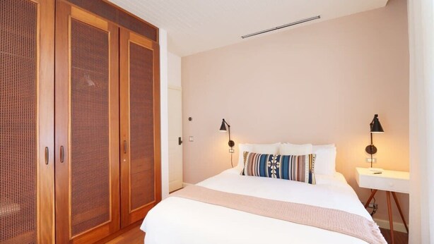 A bedroom with a bed, bedside lamps, a nightstand, and a wardrobe.