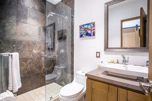Een moderne badkamer met een douchecabine van glas, een wit toilet en een houten wastafelmeubel met een wastafel.
