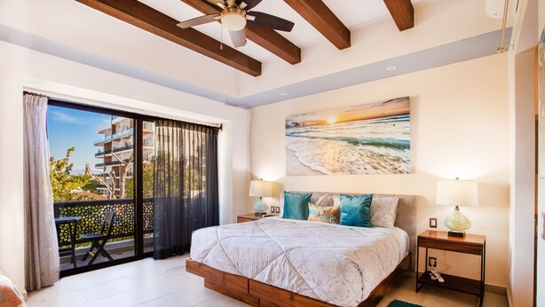 Ein Schlafzimmer mit einem großen Bett, einem Balkon mit Aussicht und einem Gemälde vom Strand.