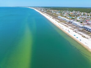 An aerial view of a coastal town with a long beach, clear water, and a mix of residential and commercial buildings. - Across the Street from Beach with Gulf Views & Community Pool in SJB (St. Joe Beach)