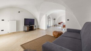 A spacious living area with a flat-screen TV, a grey sofa, and a brown ottoman. - 2982 Porta Barocca by Barbarhouse (Lecce)