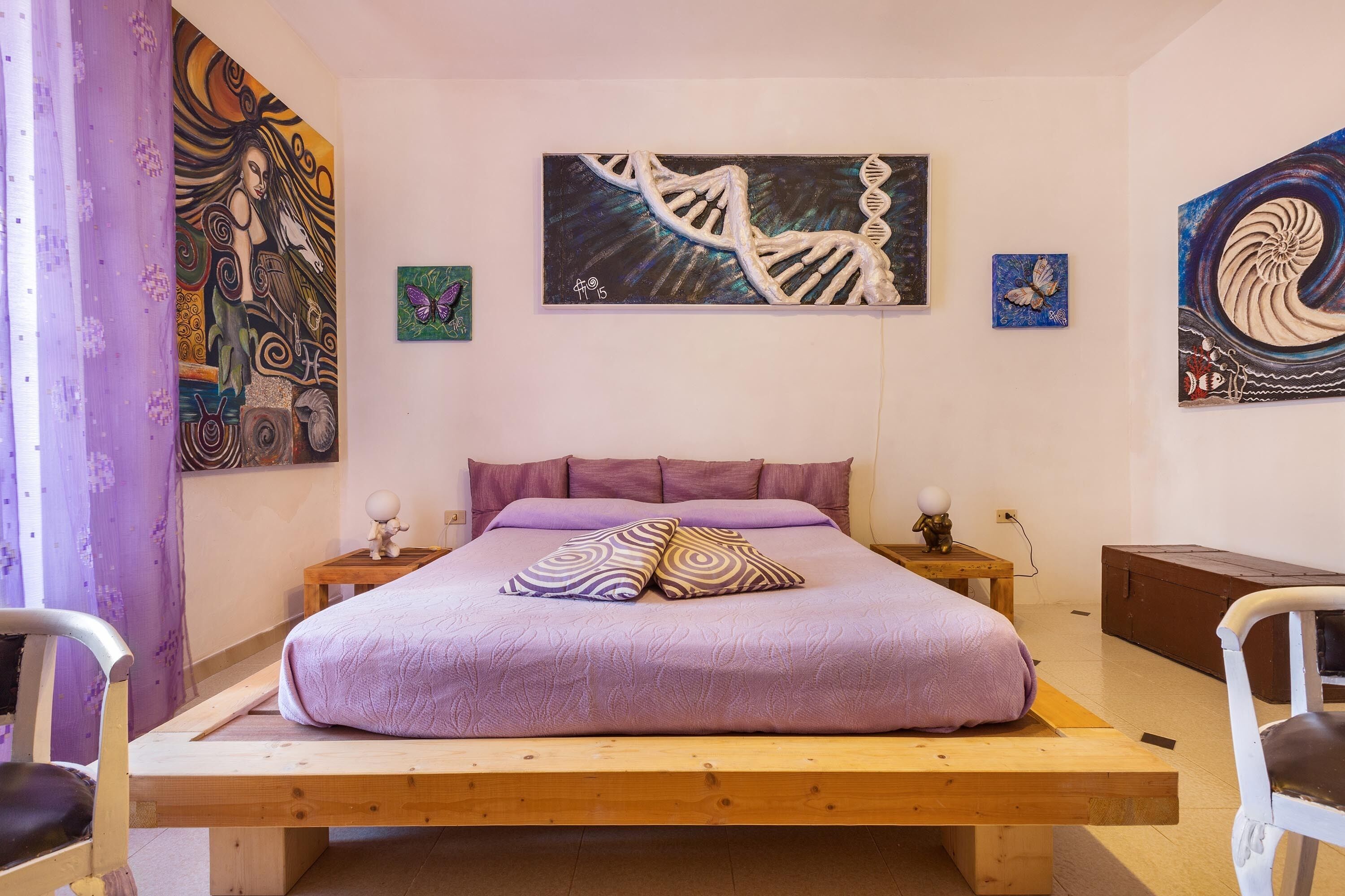 A bedroom with a wooden bed, purple bedding, and various artworks on the walls.