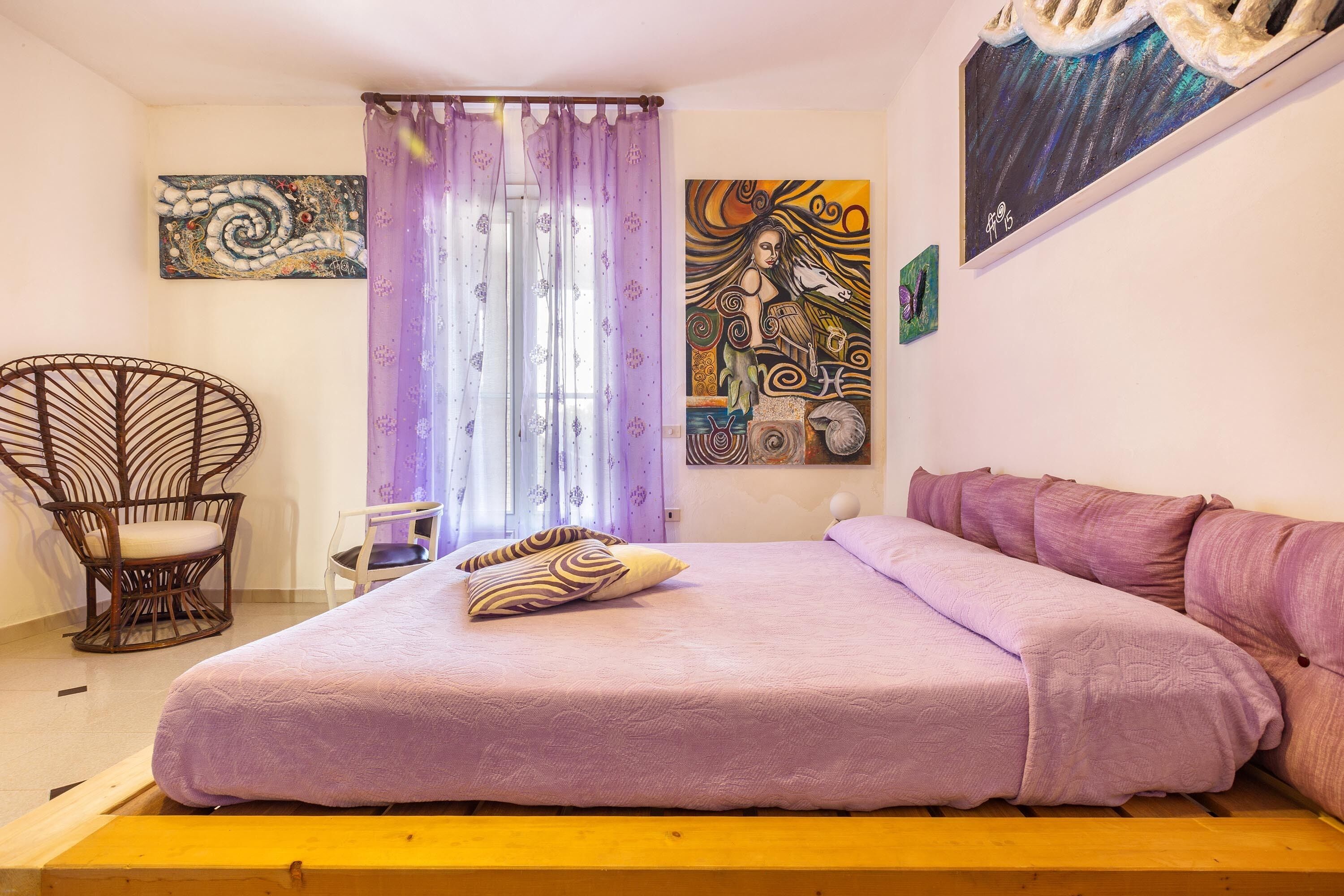 A bedroom with a bed, a chair, and artwork on the walls.