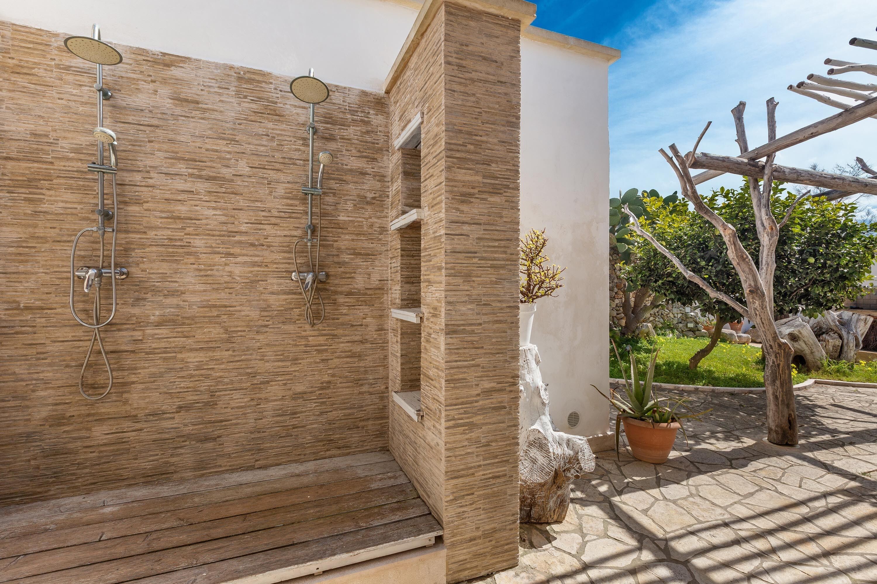 A wooden shower enclosure with a built-in bench, a potted plant, and a stone sculpture.