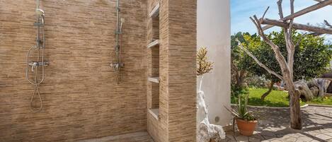 A wooden shower enclosure with a built-in bench, a potted plant, and a stone sculpture.