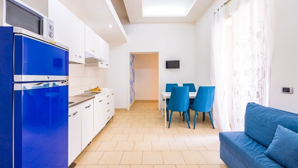 A modern kitchen with white cabinets and a blue refrigerator, a dining area with blue chairs, and a blue sofa in a bright room with a skylight. - Tribunali 194 - Cozy Flat in Center (Naples)