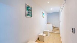 A narrow hallway with white walls, a tiled floor, and a staircase leading to an upper level. There are three small white stools aligned along the wall. - Tribunali 194 - Cozy Flat in Center (Naples)