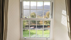 A room with a large bay window overlooking a green landscape with trees and a distant mountain range. - Slaters Rest (Ambleside)