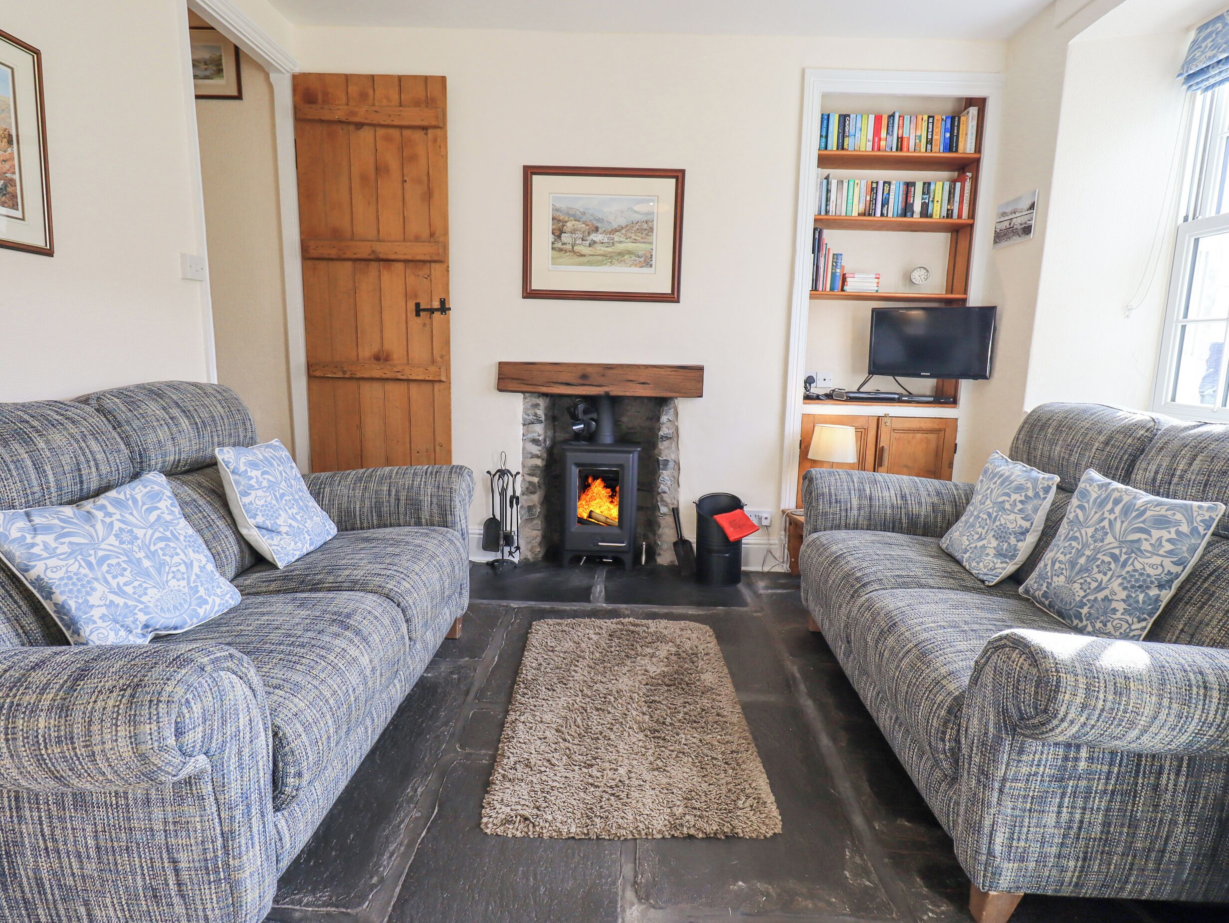 A cozy living room with two grey sofas, a fireplace, a bookshelf, and a television.