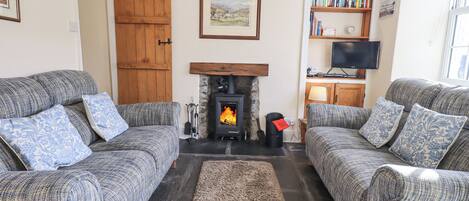 A cozy living room with two grey sofas, a fireplace, a bookshelf, and a television.