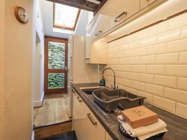 Una cocina compacta con un lavamanos integrado, un ventanal sobre la puerta y vistas a un muro de piedra a través del vidrio.
