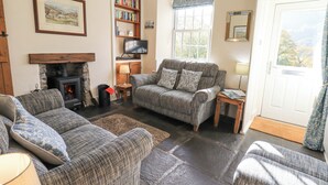 A cozy living room with a fireplace, a sofa set, a bookshelf, and a television. - Slaters Rest (Ambleside)